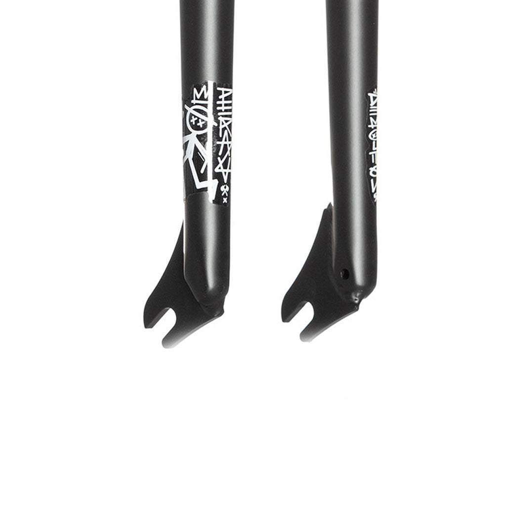 Close-up view of the dropout section of two black, heat-treated CRMO bicycle fork legs with white logo graphics; these tapered legs are part of the Demolition Peraza Forks.