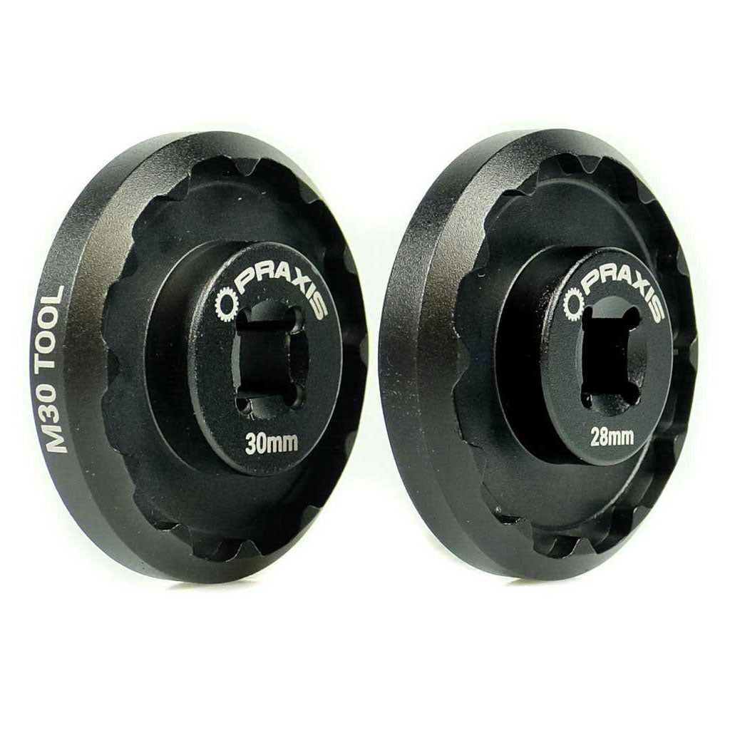 Installing a pair of black wheels using the Praxis Works M30 Standard Bottom Bracket Tool on a white background.