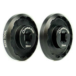 Installing a pair of black wheels using the Praxis Works M30 Standard Bottom Bracket Tool on a white background.