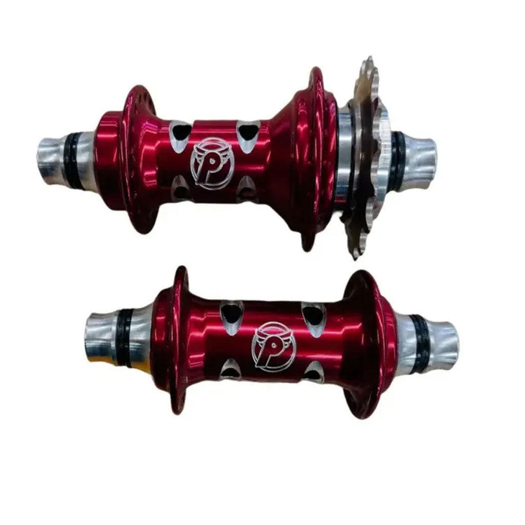 Two red anodized PROFILE Limited Edition Cat's Eye Hubs with silver axles and circular cutouts, one fitted with a silver sprocket, are displayed on a white background—perfect for standout style and top performance.