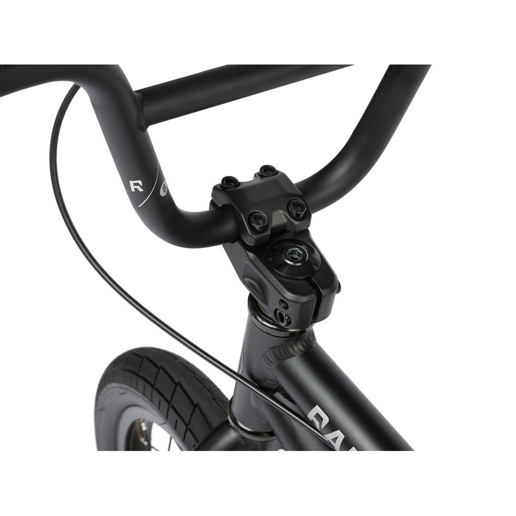 Close-up of a black Radio Dice 14 Inch Bike handlebar and front tire, showing the handlebar clamp, brake cable, and part of the lightweight 6061-T6 alloy frame.