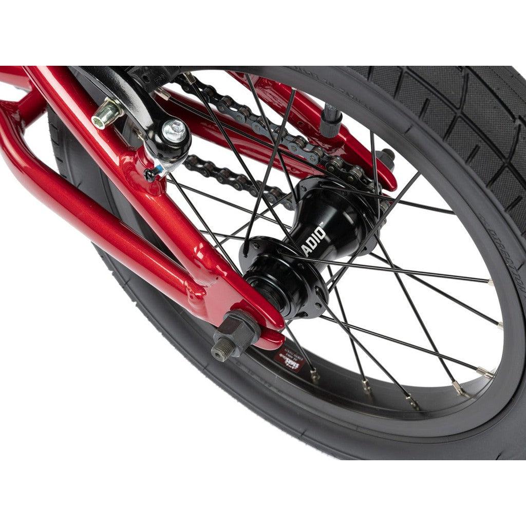 Close-up view of the rear wheel and drive mechanism of a Radio Dice 14 Inch Bike with a red 6061-T6 alloy frame, showcasing the spokes, hub, chain, and tire tread in detail.