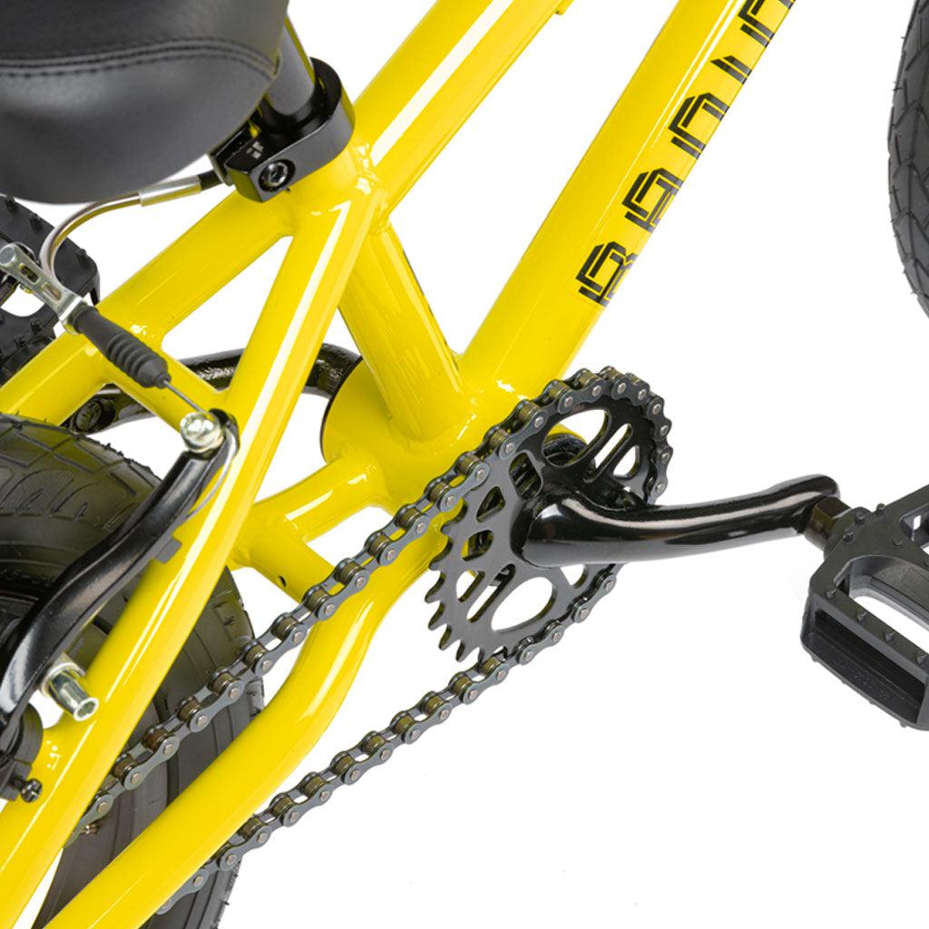 Close-up of a Radio Revo 14 Inch bike's crankset, chain, and rear tire, featuring the pedals and part of the frame.