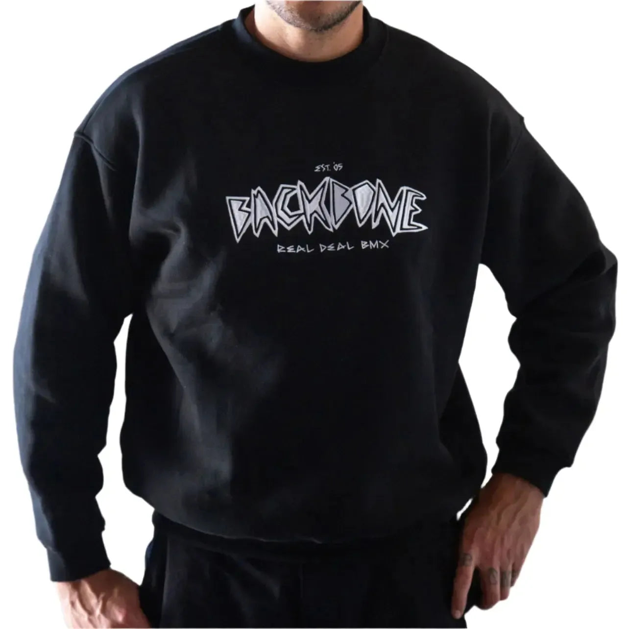 Wearing the Backbone Real Deal Crewneck—featuring "BACKBONE REAL DEAL BMX" in bold white text—against a white brick wall. This black sweatshirt is the perfect addition to your winter kit.