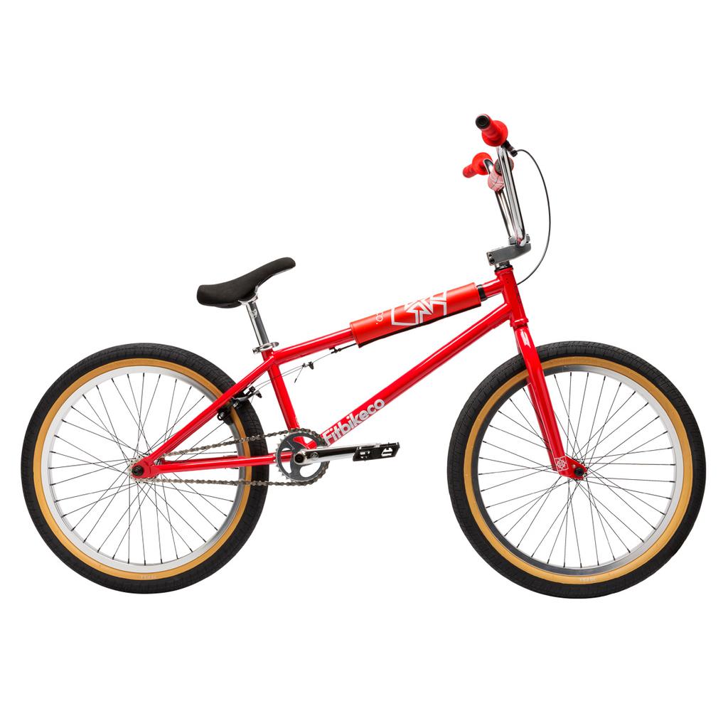 The Fit Bike Co Series 22 Inch Bike is shown in profile, featuring a red frame, black seat, black handlebars with red grips, and tan-walled tires, all set against a white background.