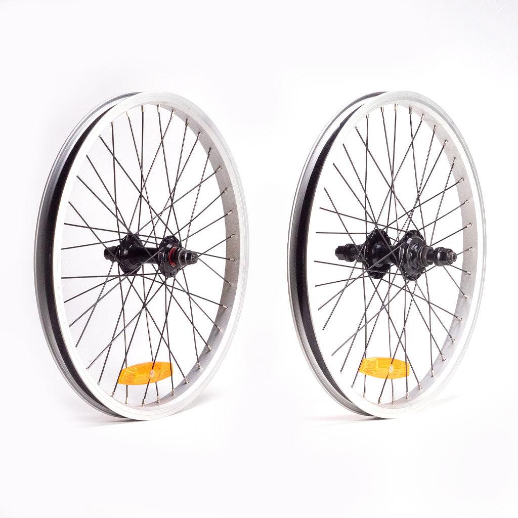 Two Redline RLD 20 B Complete wheels with black hubs, silver double wall rims, and spokes. Each wheel has a reflective yellow reflector attached to the spokes. The rear wheel features a robust RHD cassette, ensuring smooth gear shifts for your ride.