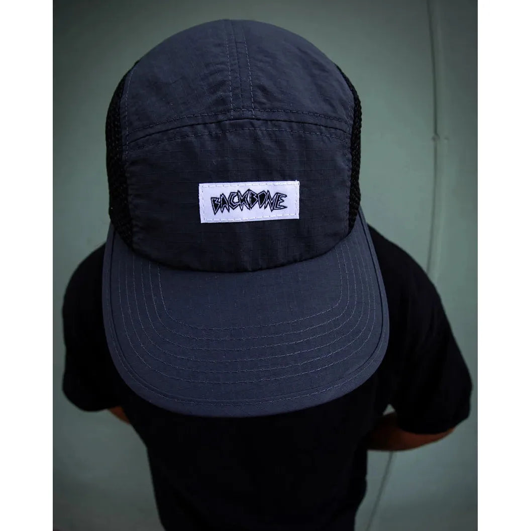 A person wearing a Backbone Ride Club Hat—black with a white “BACK2DIME” patch—viewed from above, against a plain green background.