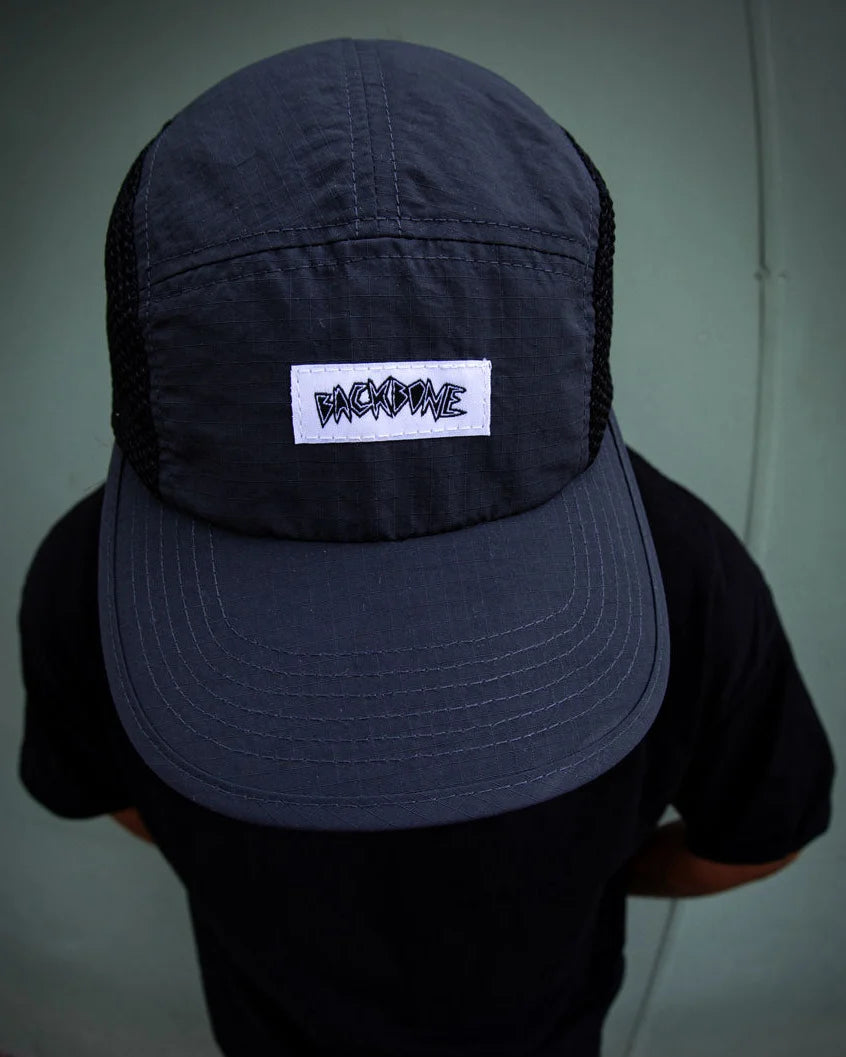A person wearing a Backbone Ride Club Hat—black with a white “BACK2DIME” patch—viewed from above, against a plain green background.
