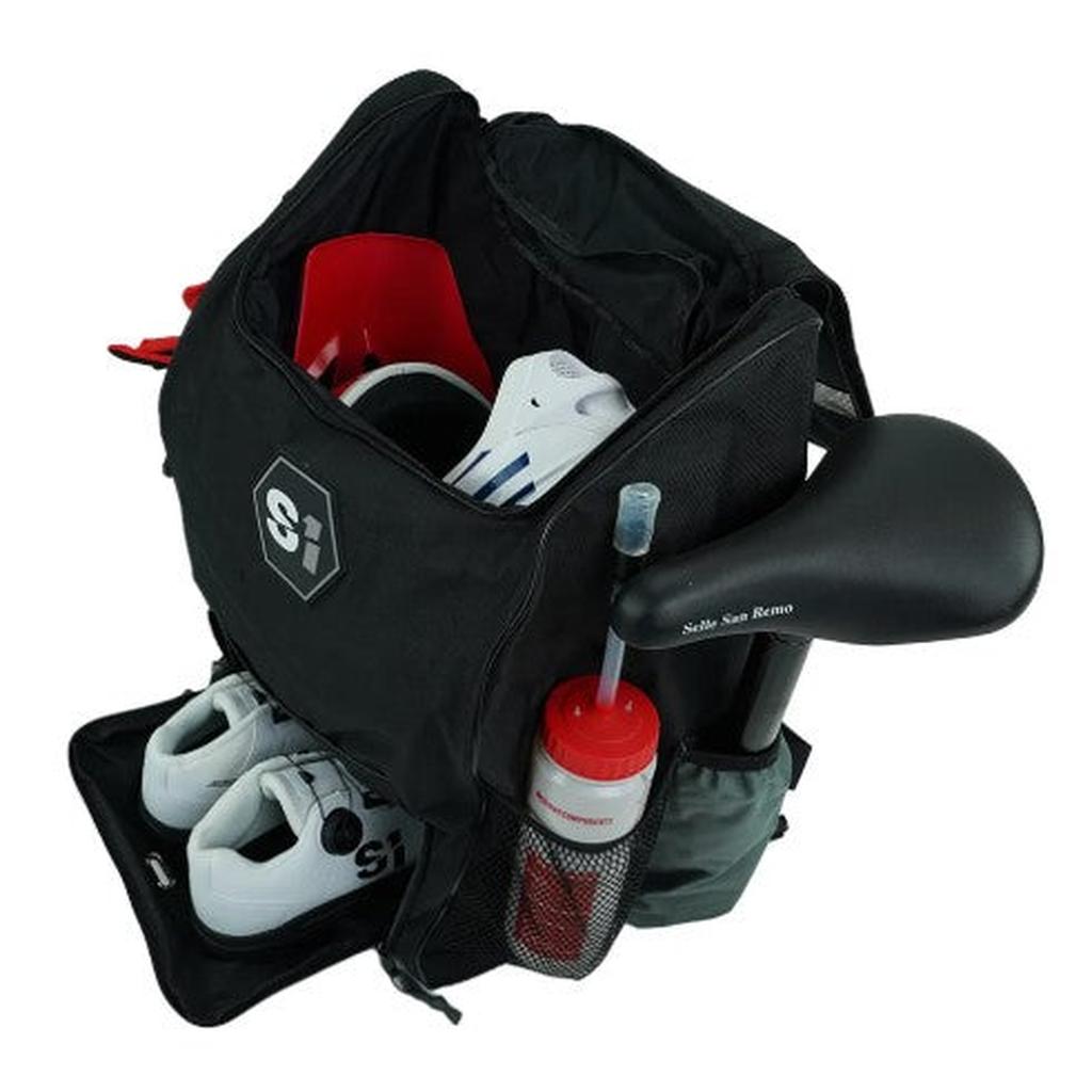 Open black S1 Helmet / Gear Backpack holding cycling shoes, a helmet, a water bottle in the side pocket, and a partially inserted bicycle saddle.