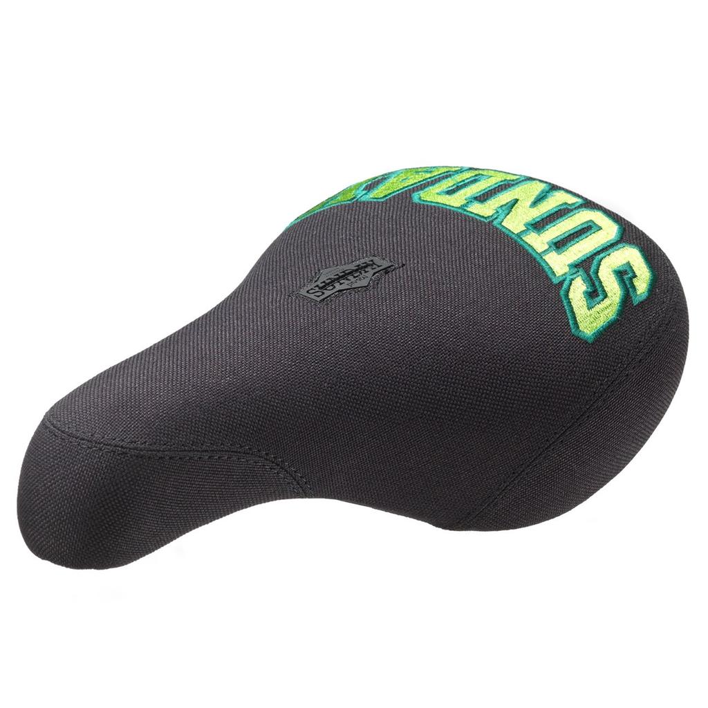 The Sunday Blockhead Pivotal Seat is a black bike seat featuring green and yellow "SUNDAY" embroidery and a small Sunday Bikes logo tag, adding unique style to your ride.