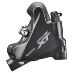 Close-up of the Shimano Deore XT Flat Mount Disc Brake Caliper in matte black, showcasing the branding, detailed hardware, and a portion of the disc brake rotor.
