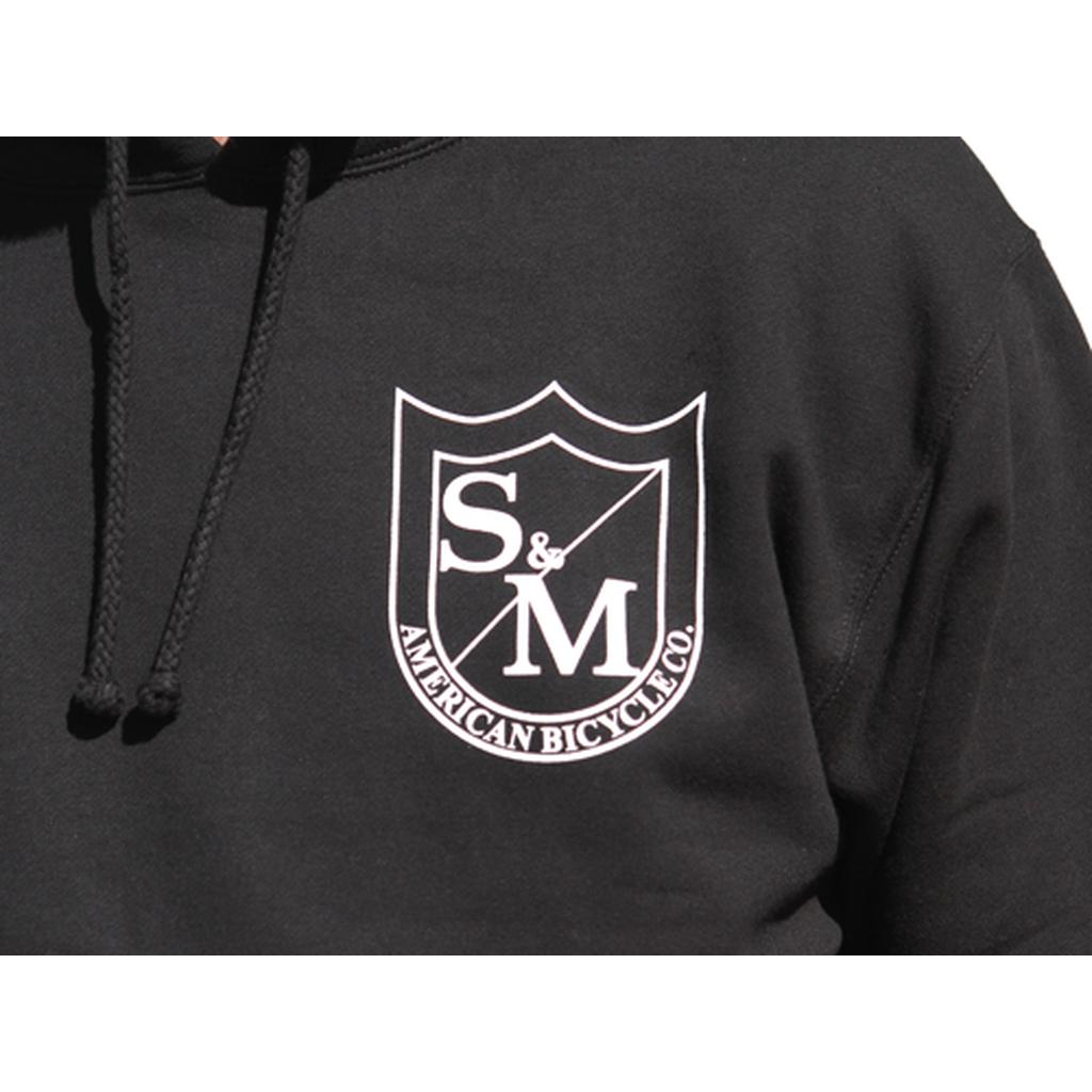 The S&M Two Shield Pullover Hoodie features a white shield logo with "S & M American Bicycle Co." on the chest, a cozy fleece-lined hood, and is crafted for comfort—sweet hoods, printed in the USA.
