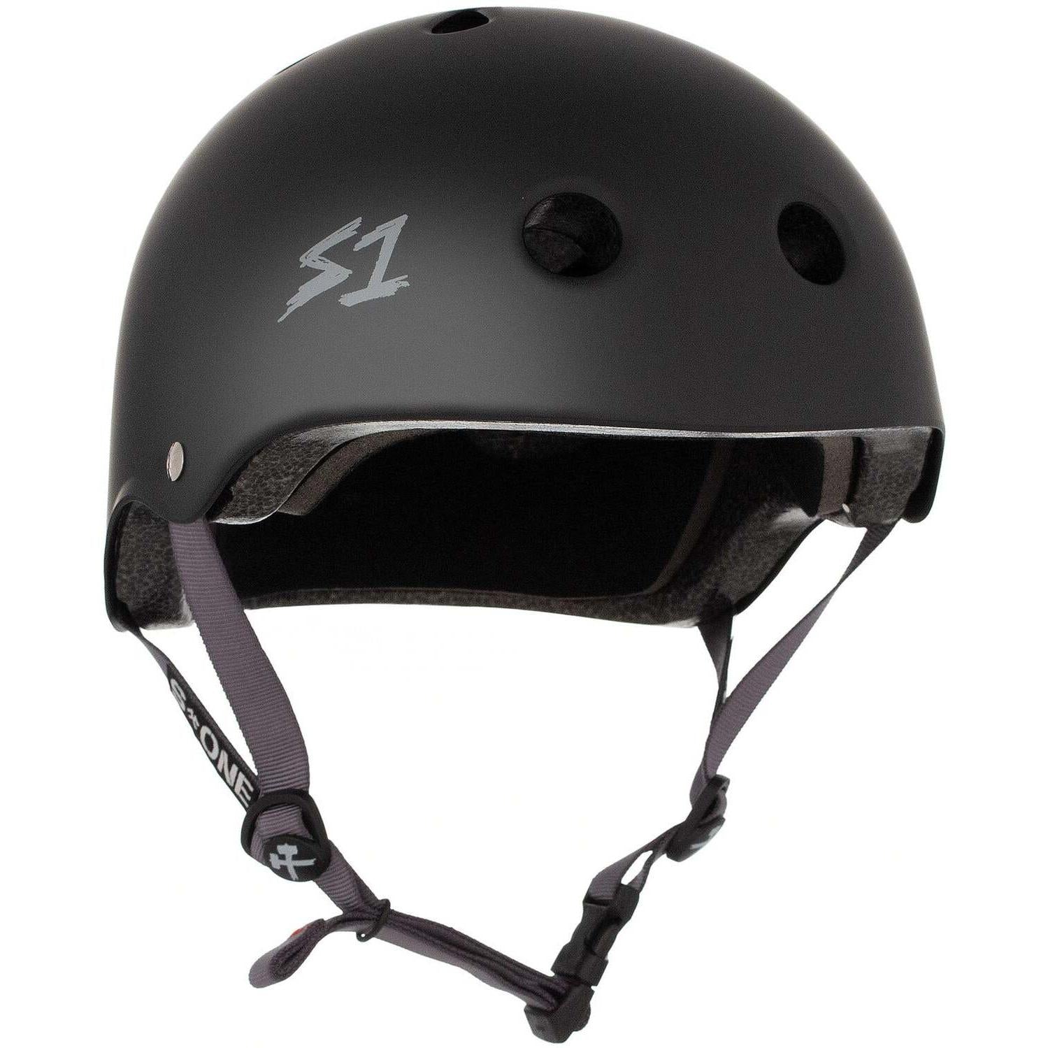 The S-One Lifer Helmet in black matte with grey straps features ventilation holes, an adjustable chin strap, a certified skate helmet design, and side "S1" logo for multiple impact protection.