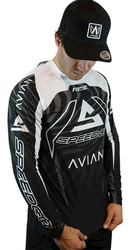 A man in the Speedco / Avian Race Jersey with an aerodynamic fit and a black cap, both displaying the AVIAN and SPEEDCO logos, stands with hands in front—embodying focused race-day apparel style.