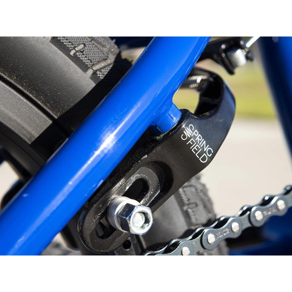 Close-up of the Sunday Blueprint 16 Inch Bike’s rear dropout showing a chain tensioner, part of the chain and tire, and Odyssey Springfield Brakes with "SPRINGFIELD" printed on the black metal component.