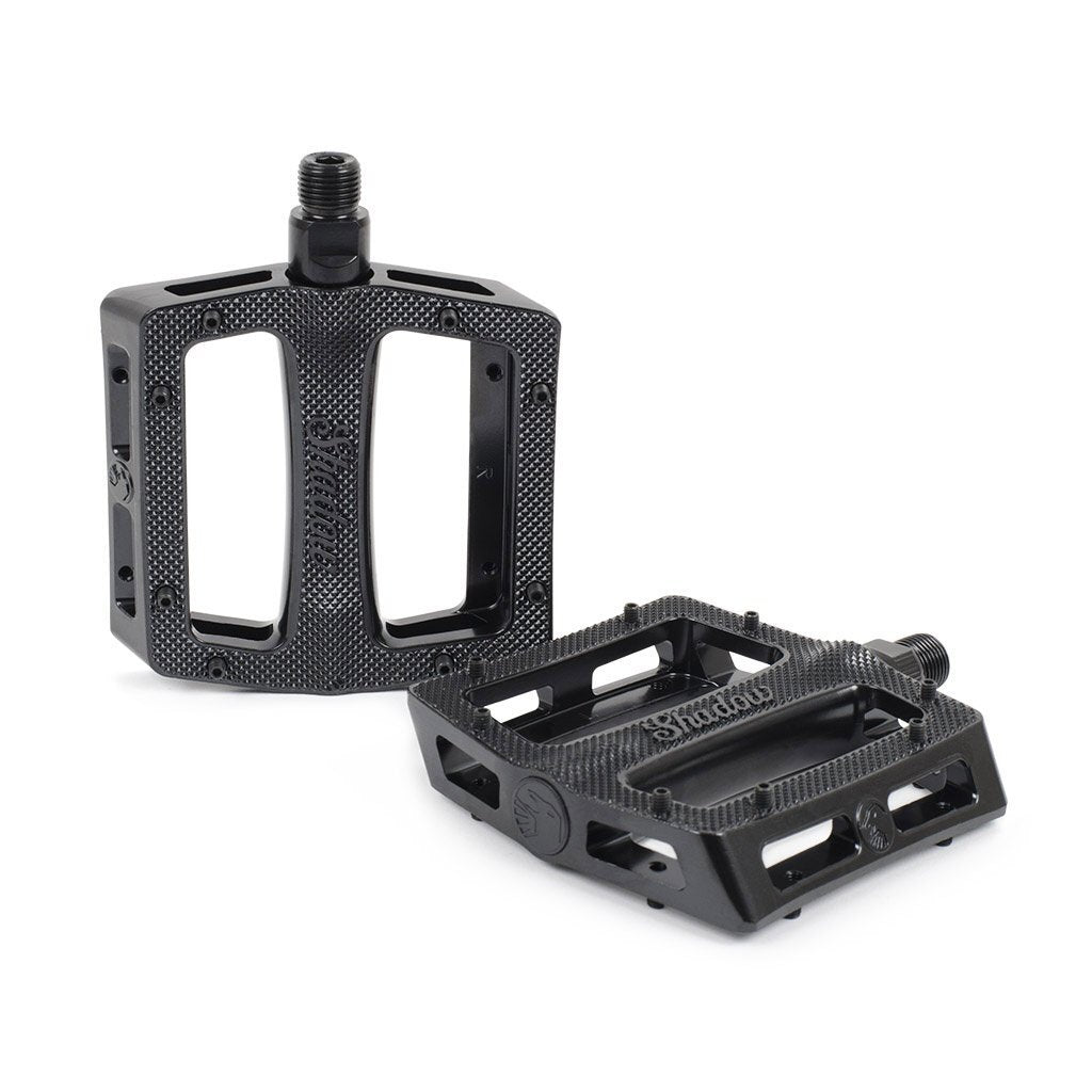 The Shadow Metal Sealed Pedals are black alloy pedals featuring a slim body, textured surfaces, and open rectangular frames. They can be positioned both upright and flat.