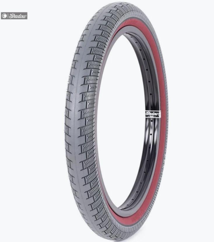The Shadow Creeper 20 Inch Tyre is a high psi street and park tire featuring a black tread, red sidewall, and black rim, displayed upright against a white background.