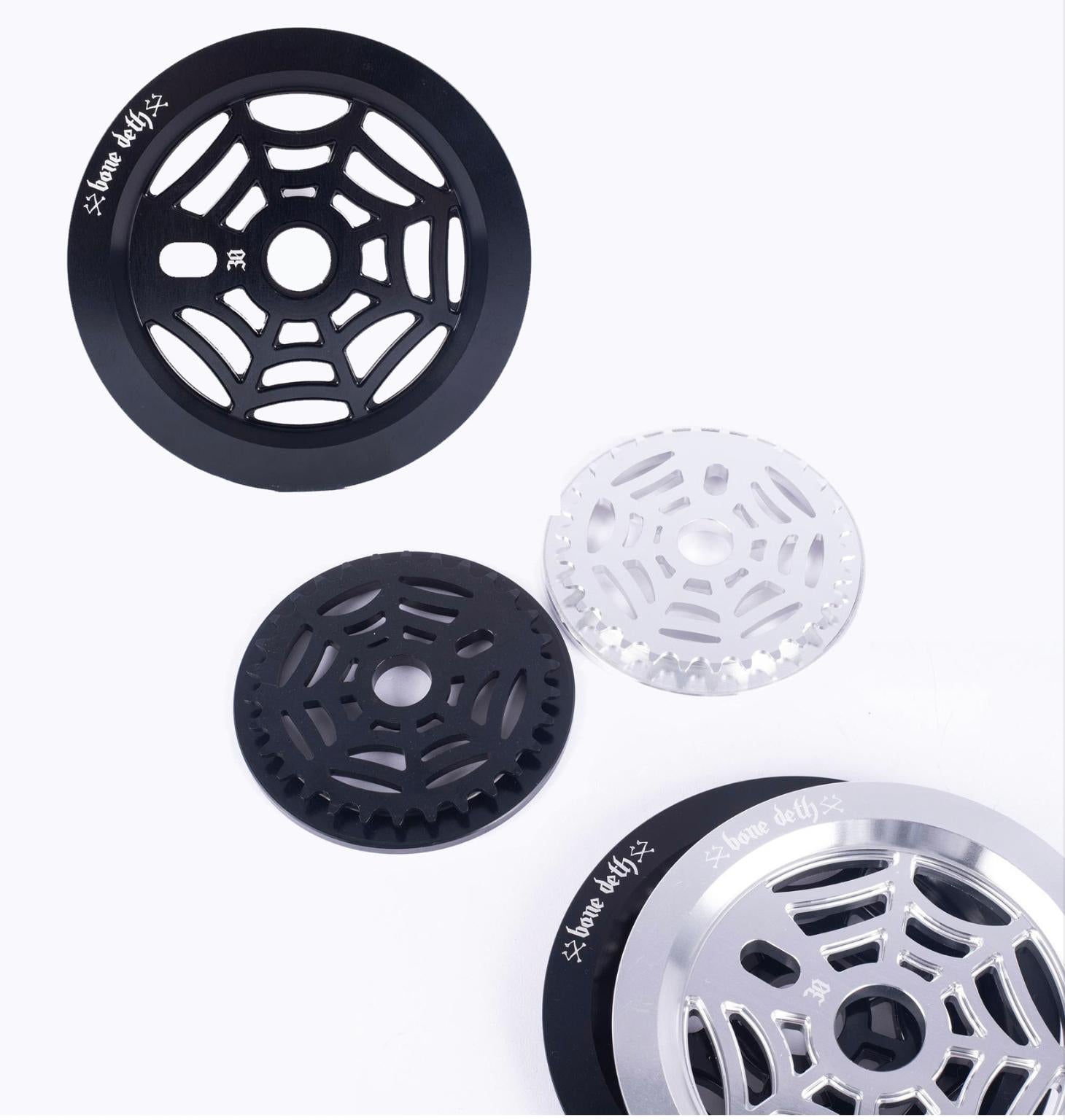 Four BMX sprockets, featuring the Bone Deth Webslinger design, are set against a white background. Each displays unique web-like patterns and vibrant colors, enhancing your ride's style.