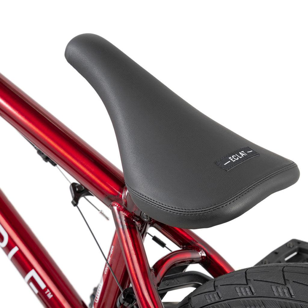 Close-up of a black "ECLAT" seat on a Wethepeople Versus 20 Inch Bike with a red Chromoly frame, showing part of the rear tire.
