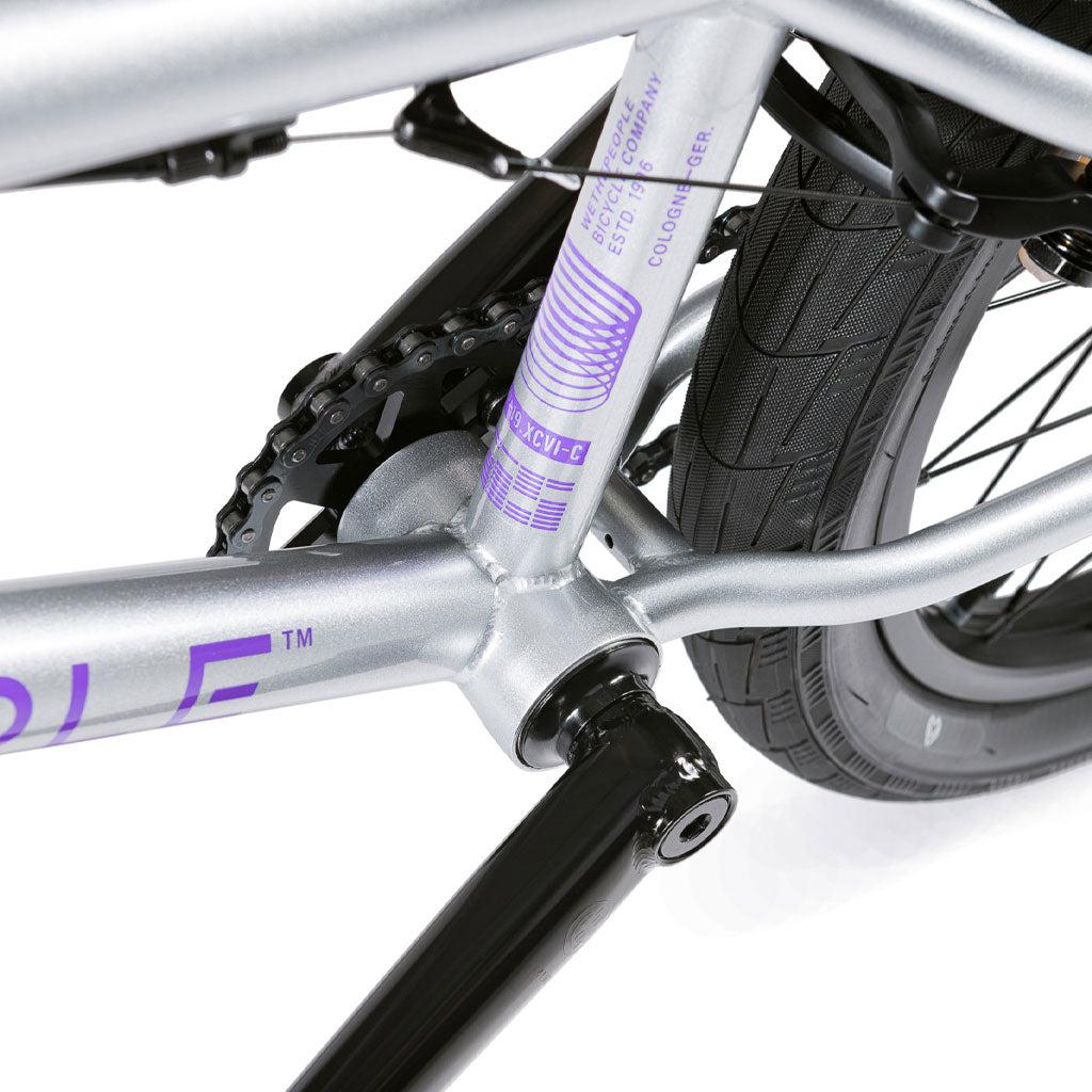 Close-up of the Wethepeople Versus 20 Inch Bike, featuring its silver Chromoly frame, detailed rear wheel, chain, and crank components against a white background.