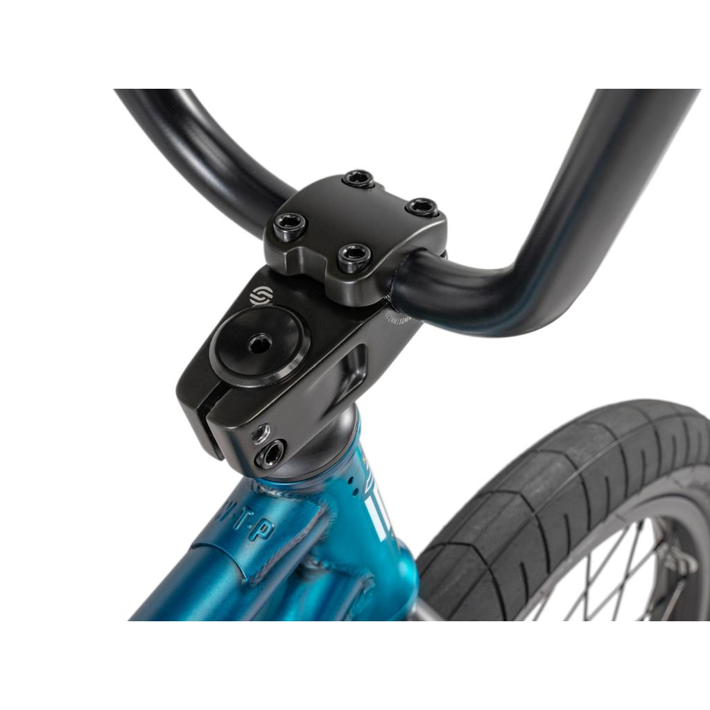 Close-up of the Wethepeople Arcade 20 Inch Bike's black Salt Comp handlebar stem mounted on its blue frame, with the front wheel and thick tire visible.