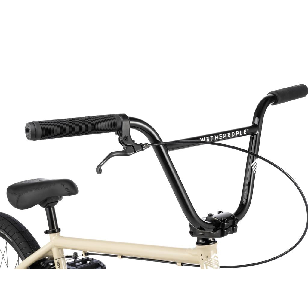 Close-up of the Wethepeople Arcade 20 Inch Bike’s black handlebars with a Salt Comp brake lever and cable, featuring the "We The People" logo near a black saddle—designed for style and performance.