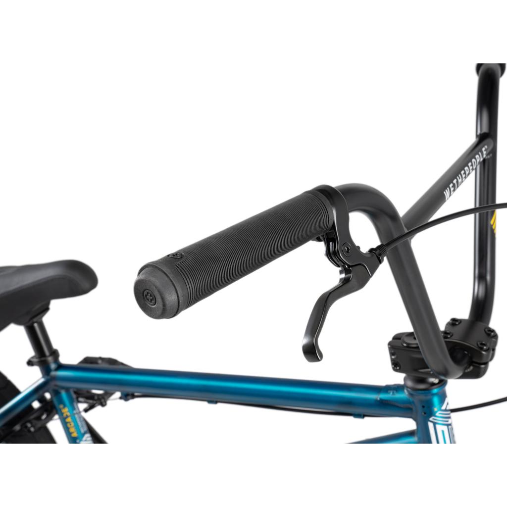 Close-up of a black handlebar with textured rubber grip and brake lever, attached to the blue Wethepeople Arcade 20 Inch Bike frame featuring Salt Comp components.