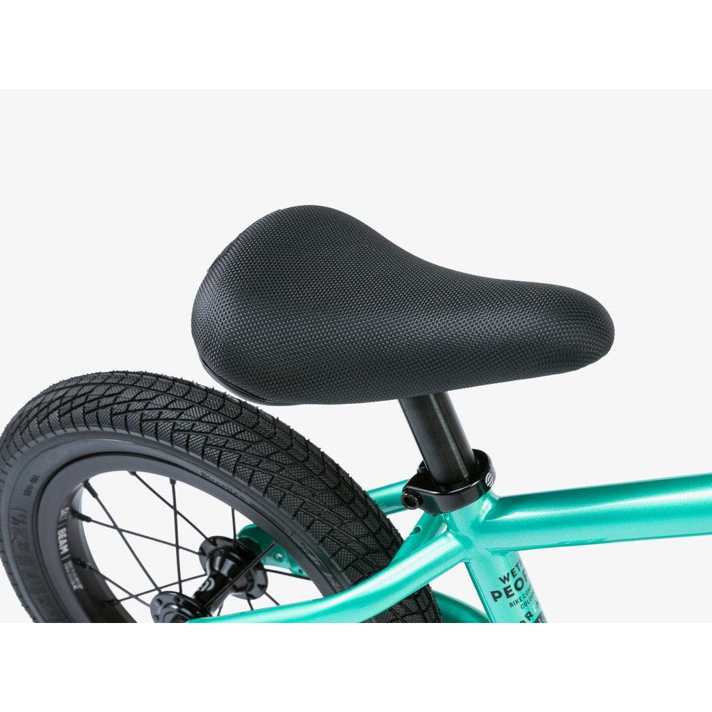 Close-up of a black bike seat on a teal Wethepeople Prime 12 Inch Balance Bike frame, with part of the rear wheel and tire visible.