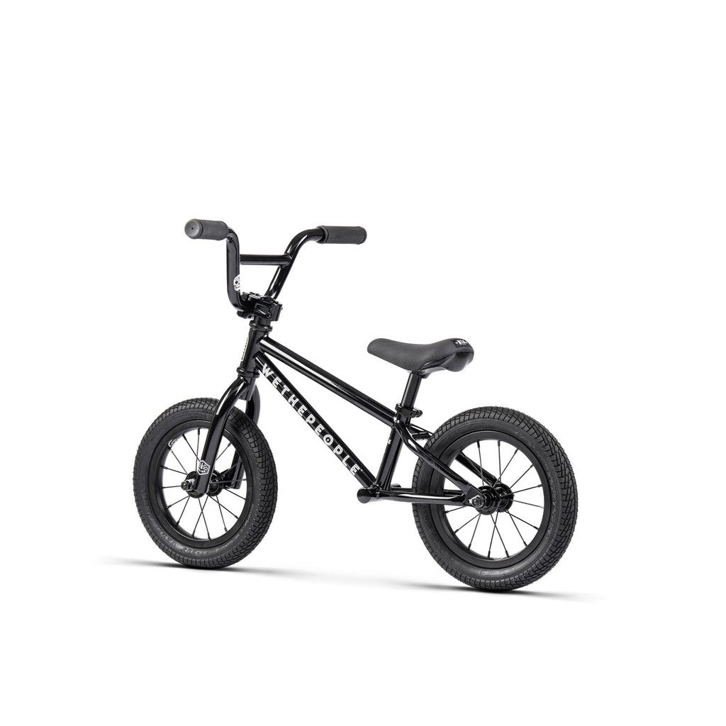A Wethepeople Prime 12 Inch Balance Bike in black with thick tires, a padded seat, and "Wethepeople" branding on the frame, displayed against a white background.