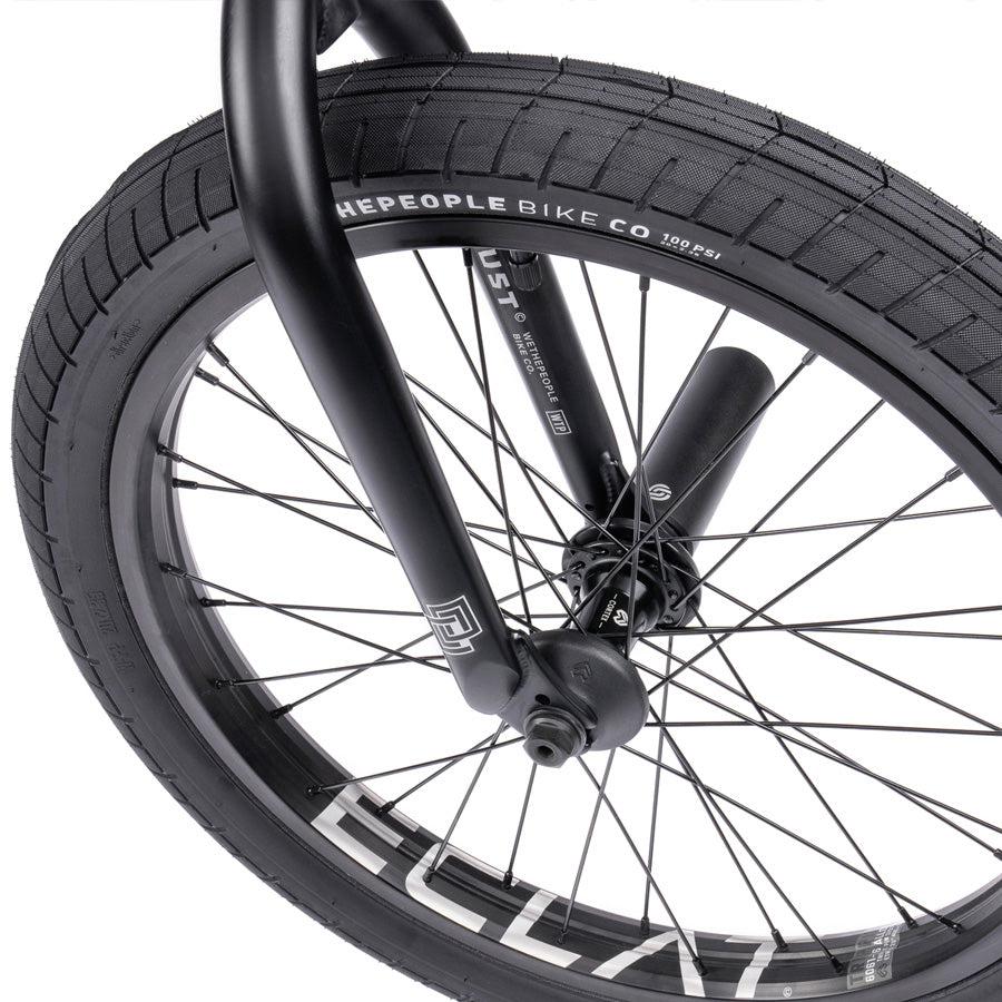 Close-up of the front wheel on a BMX bike, highlighting black spokes and a tire labeled "WETHEPEOPLE BIKE CO," with visible inflation details and battleship geometry from the Wethepeople Trust 20 Inch Freecoaster/Hybrid Bike.