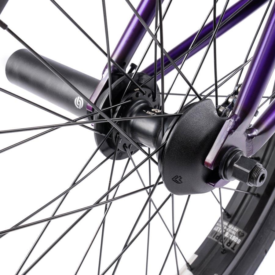 Close-up view of the Wethepeople Trust 20 Inch Freecoaster/Hybrid Bike wheel with a purple frame, showcasing the hub, spokes, and axle nuts.