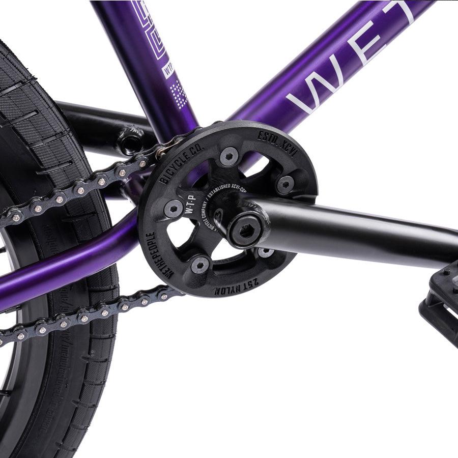 Close-up of the Wethepeople Trust 20 Inch Freecoaster/Hybrid Bike's purple frame, chainring, and crankset with a black pedal, showcasing its distinctive battleship geometry.