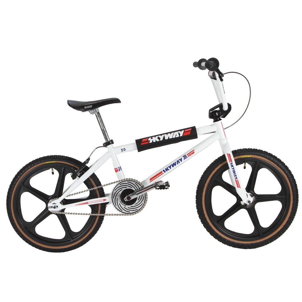 The Skyway TA 20 Replica 20 Inch Bike (2026) is a white BMX with black Skyway branding, black mag wheels, Redline Flight cranks, a padded top tube, and red and blue accent stripes.