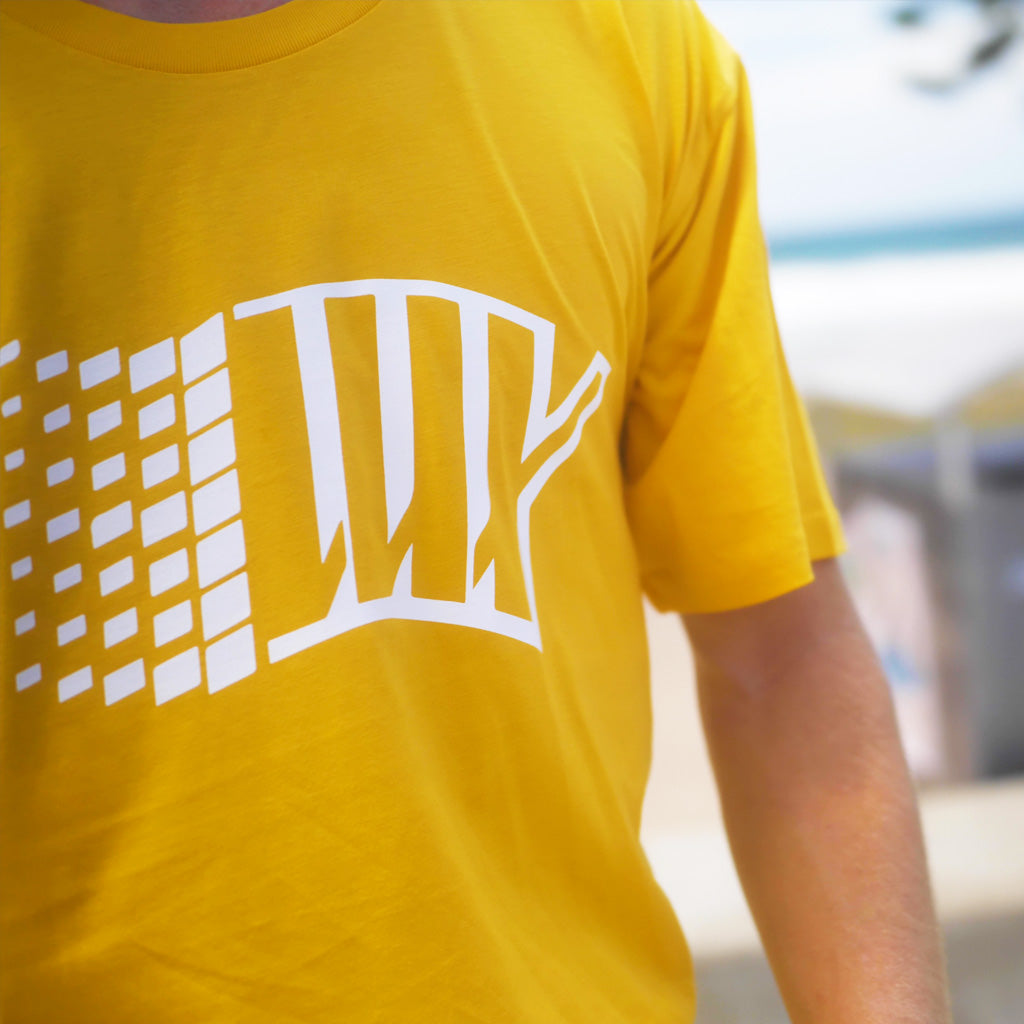 A man wearing a LUXBMX Y2K Tee - Yellow on the beach.